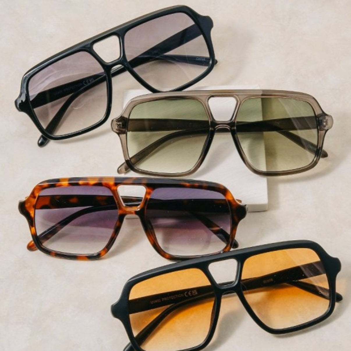 Four pairs of sunglasses with different designs and color lenses on a light background