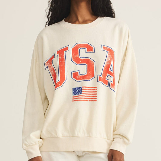 Woman wearing a cream sweatshirt with 'USA' and an American flag design on a plain background