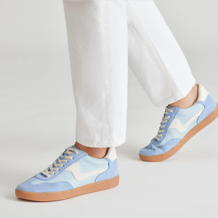 Light blue sneakers with white accents worn with white pants on a light gray background