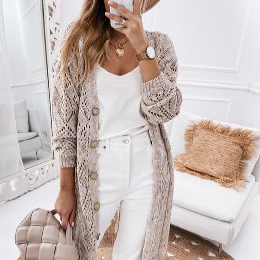 Woman taking a mirror selfie wearing a beige cardigan, white top, and pants in a stylish room.