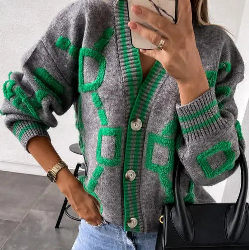 Person wearing a gray cardigan with green patterns, holding a phone, and carrying a black handbag.