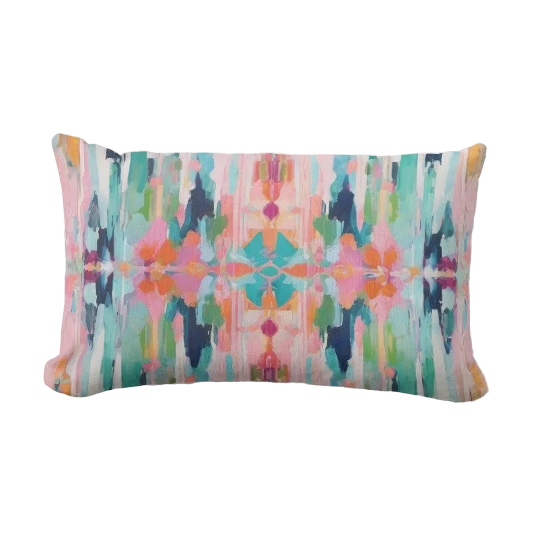 A rectangular lumbar throw pillow featuring a vibrant, symmetrical abstract watercolor pattern in pink, teal, green, orange, and navy on a light gray background.
