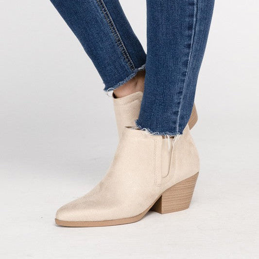 Beige ankle boots worn with blue jeans on a light gray background