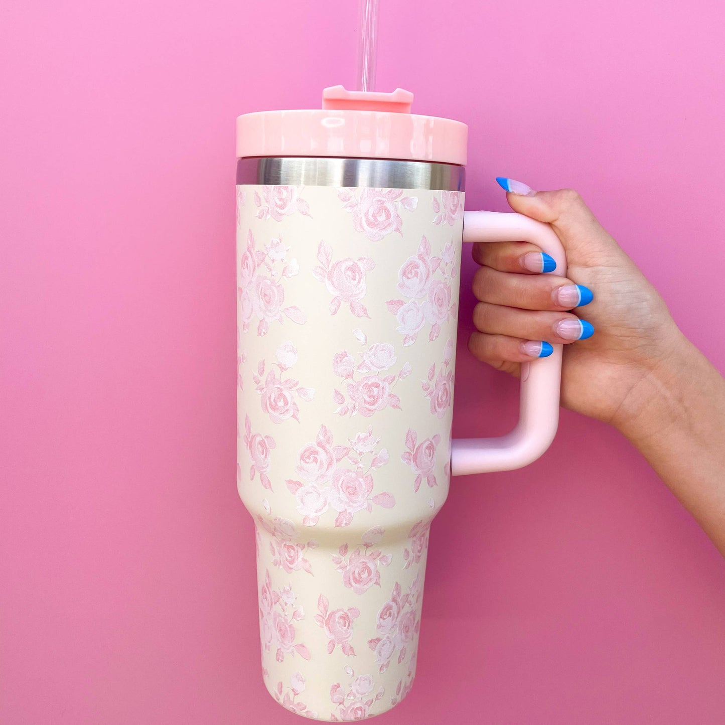 Large floral-patterned tumbler held by a hand against a pink background