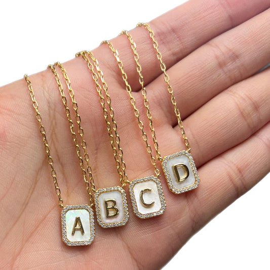 Gold necklaces with letter pendants 'A', 'B', 'C', and 'D' on a hand.