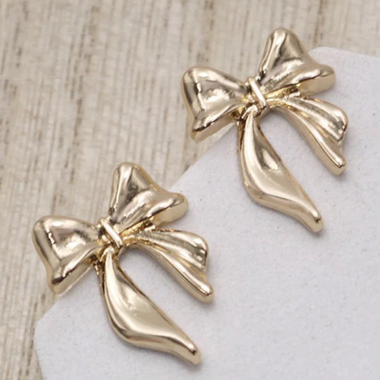 Gold bow-shaped earrings on a white stone surface with a wooden background