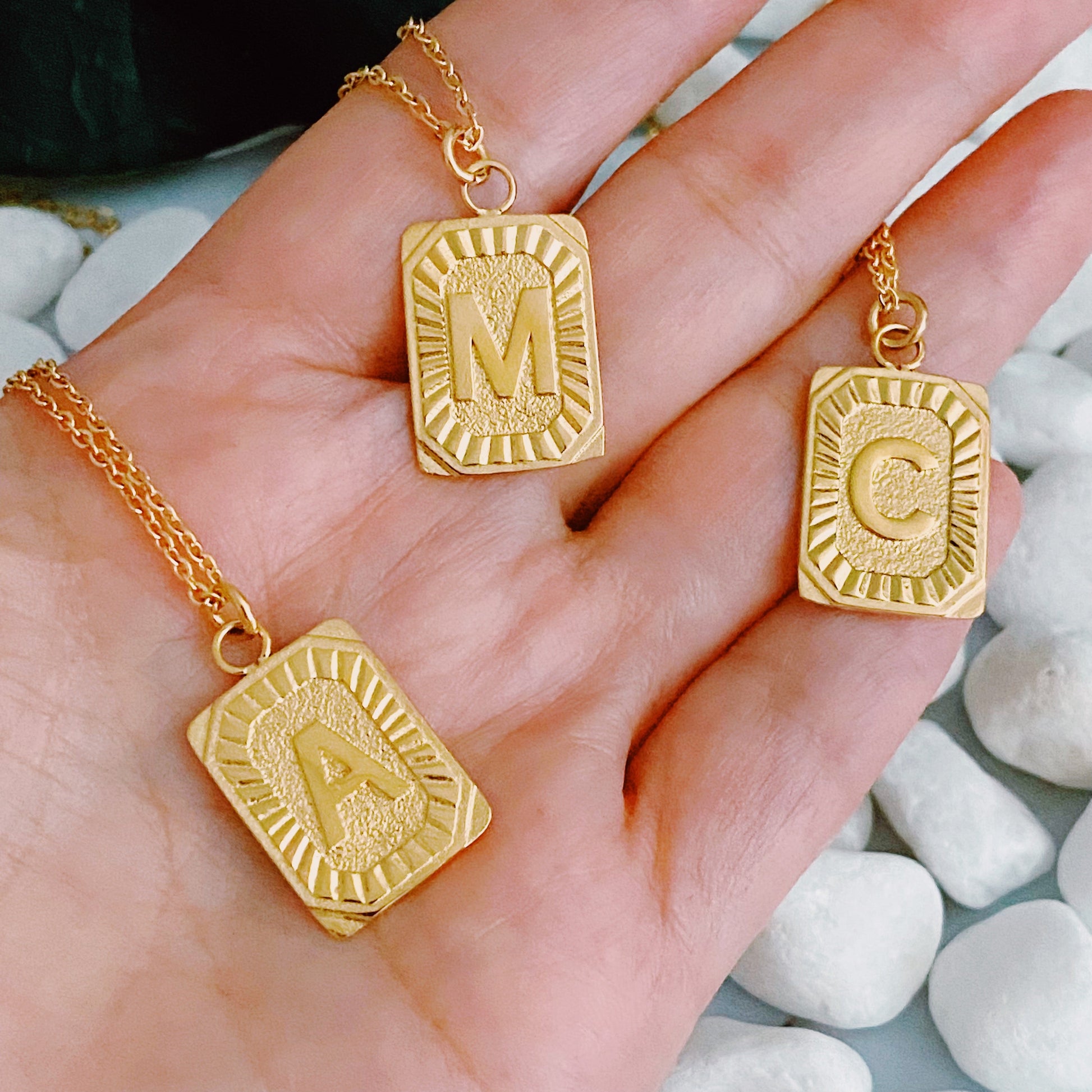 Gold necklaces with letter pendants held in a hand against a stone background