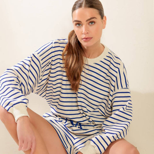 Woman wearing a blue and white striped dress sitting on a box with a plain background