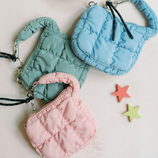 Three small fabric bags in pink, blue, and green on a light surface with colorful stars.