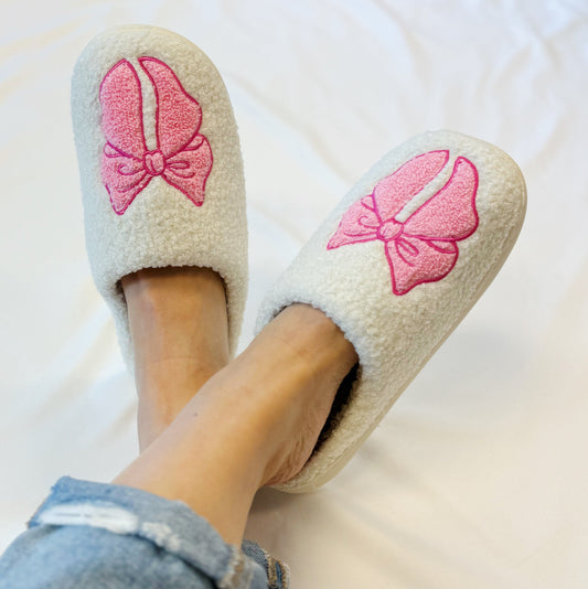 White slippers with pink butterfly designs worn by a person on a white background