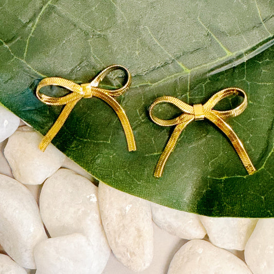 Gold bow-shaped earrings on a green leaf with white stones below
