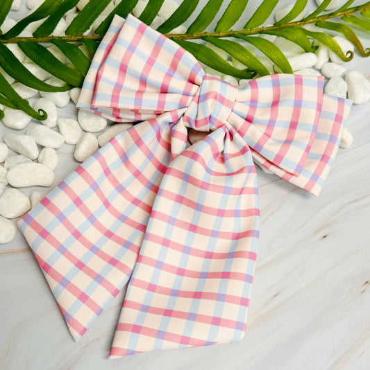 Pastel plaid bow on a light wooden surface with green leaves and white stones in the background
