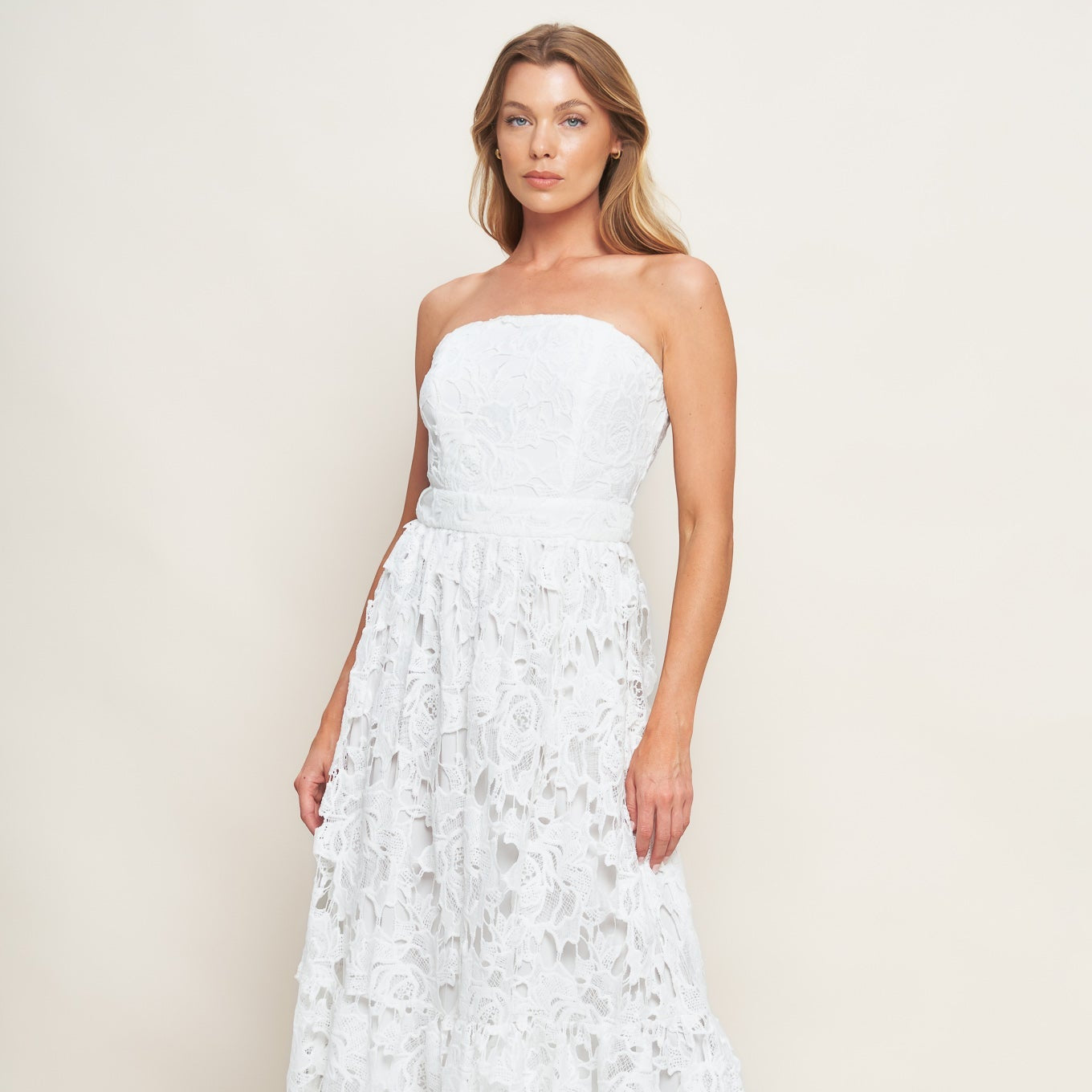 Woman wearing a white strapless lace dress against a plain background