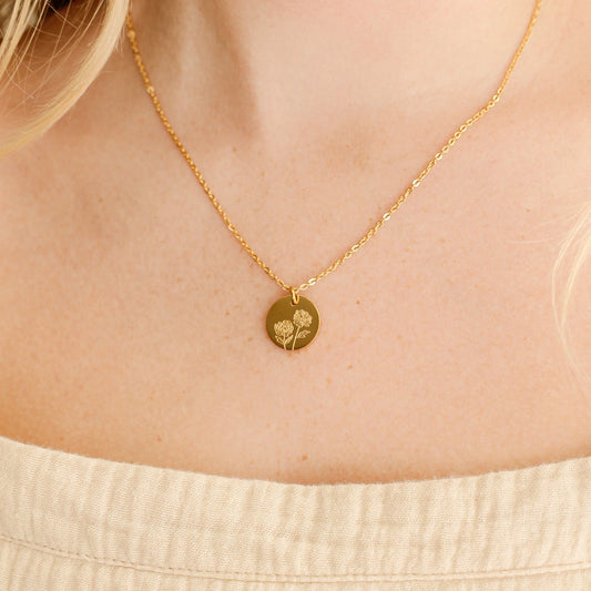 Gold necklace with a small pendant on a person wearing a beige top.