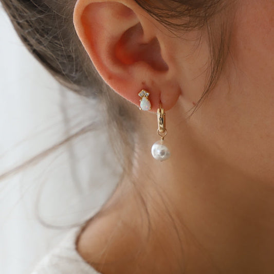 Close-up of a person wearing gold hoop earrings with pearl-like stones.