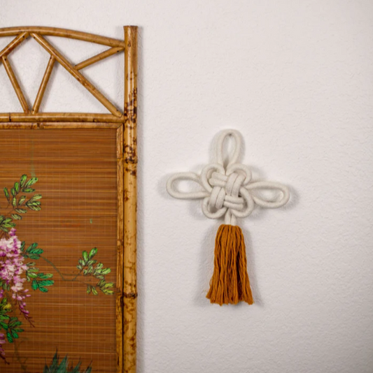 Decorative wall hanging with tassel next to a bamboo screen on a light gray background