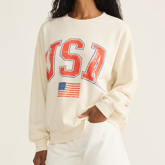 Woman wearing a cream sweatshirt with 'USA' and an American flag design on a plain background