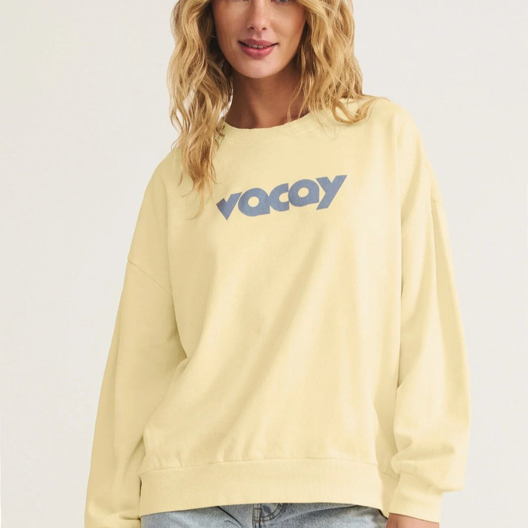 Woman wearing a light yellow sweatshirt with 'Voyag' text on a plain background